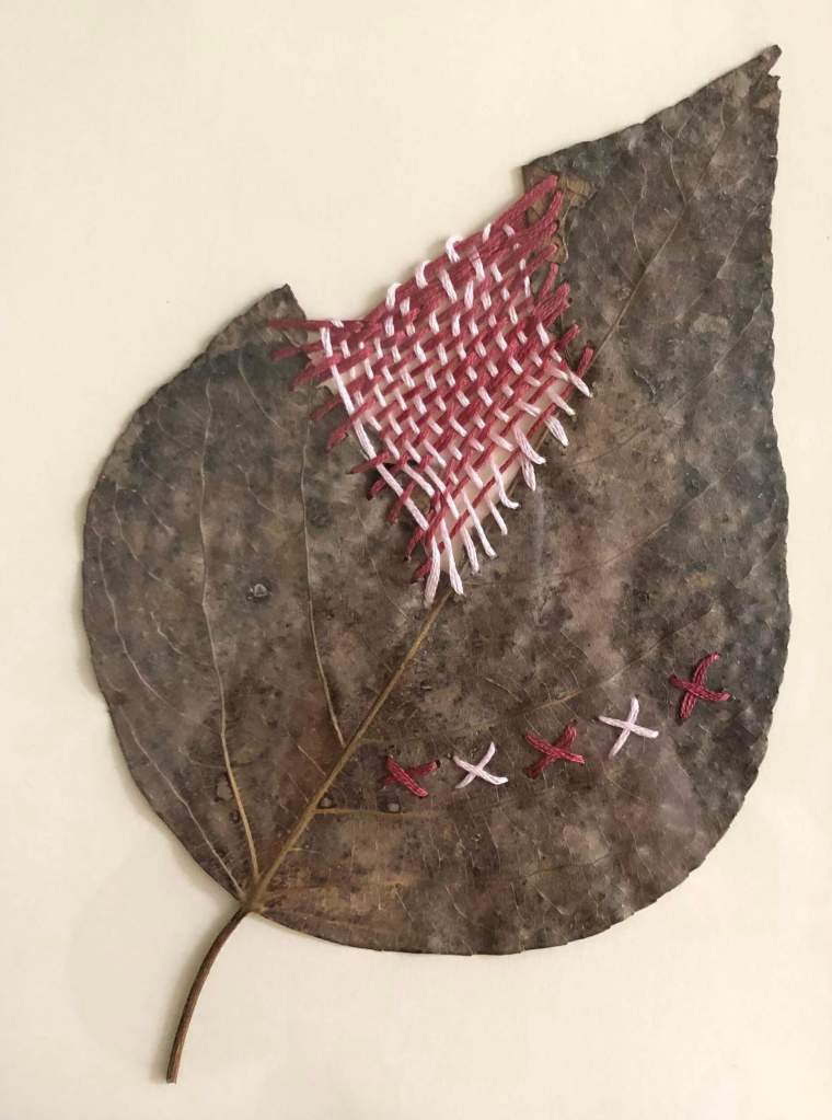 Real leaf hand embroidered pink and red using cross stitch and weaving in to repair a missing piece.