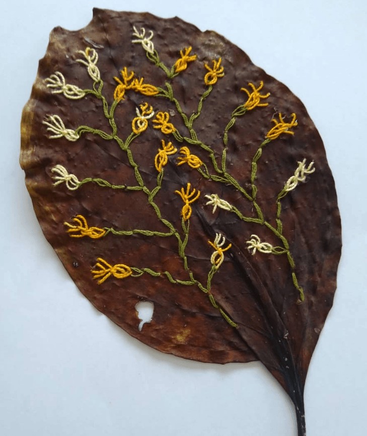 Real leaf hand embroidered using stem stitch in green and wheatsheaf stich in cream and orange to create flower design.