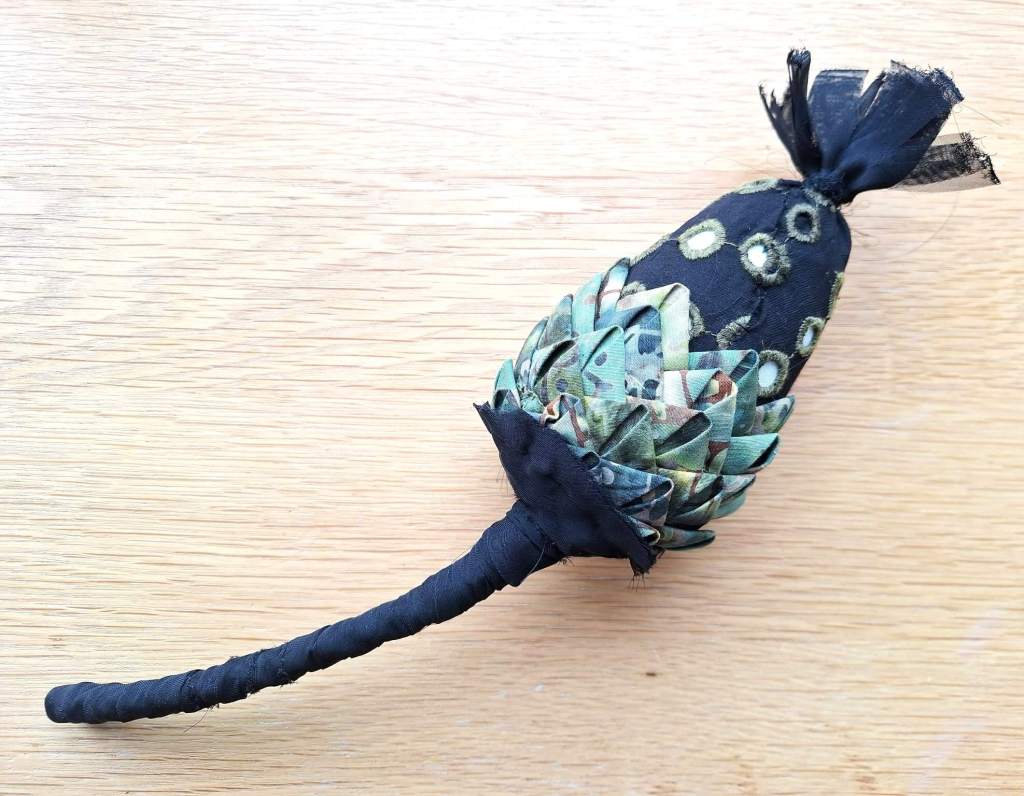 Textile abstract 3D seed pod sculpture with a long stem using fabrics and embroidery in black and shades of green.
