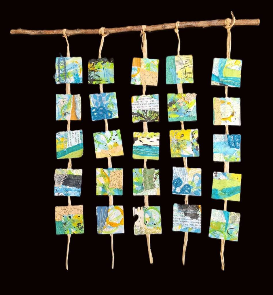 25 squares suspended from a branch with raffia. Squares are mixed media collage using paint, fabric and papers in blues, greens, sand and black.