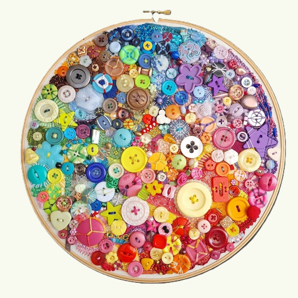 Buttons beads and embroidery stitches in a rainbow of colours sewn onto fabric in an embroidery hoop.